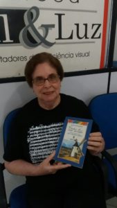 Foto da ledora Marilda Manhães segurando o livro impresso ao qual foi ledora