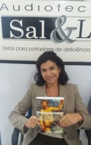 Foto de Valéria Siniscalchi segurando o livro sentada e sorridente