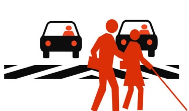 Imagem de um casal atravessando a rua e dois carros ao fundo aguardando antes da faixa de pedestre